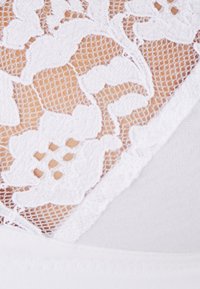Tela de encaje blanco con un patrón floral superpuesto sobre un material blanco suave, que presenta un intrincado bordado y contrastes de textura.