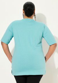 T-shirt di un azzurro chiaro con maniche corte, scollatura rotonda e spacchi laterali all'orlo. Il tessuto appare morbido e ha una vestibilità comoda.