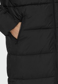 Svart pufferjakke med en blank tekstur, som har en sidelukkinglomme og brodert paneldesign, som gir varme og en praktisk stil.
