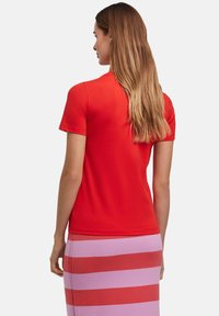 Rode t-shirt met korte mouwen van katoen met een gladde textuur, gedragen met een roze gestreepte rok. De halslijn is klassiek en rond.