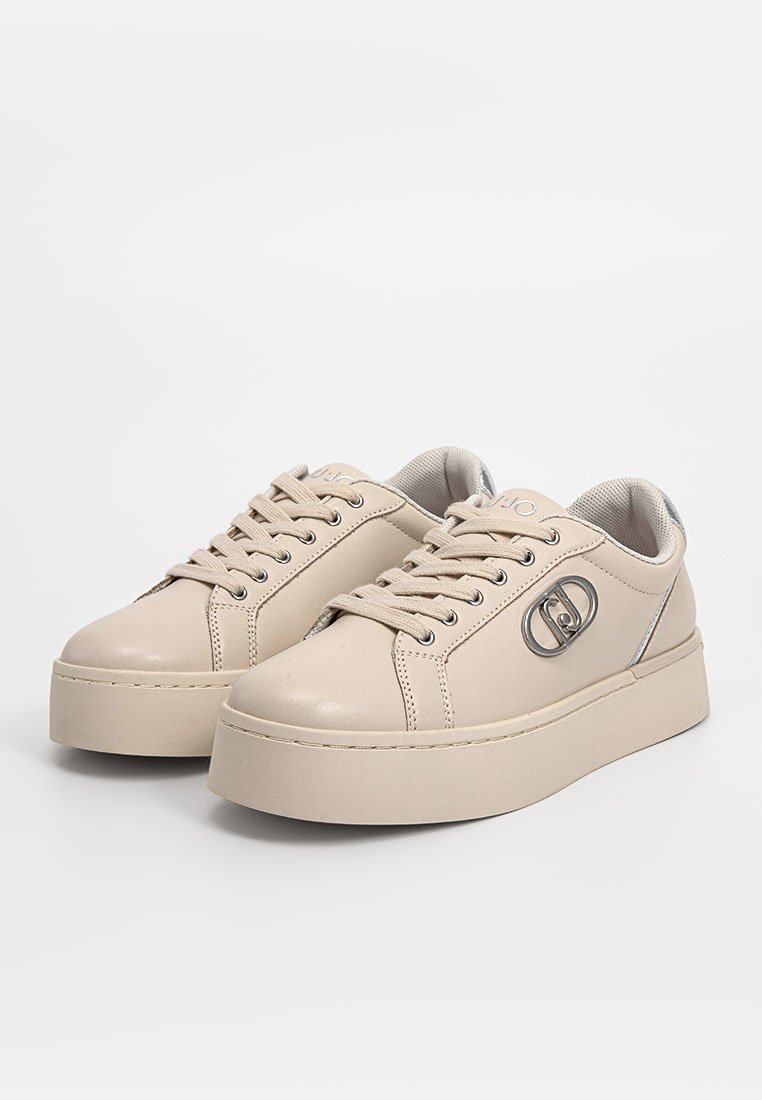 Zapatillas de cuero beige con un acabado texturizado, punta redondeada, suela plana y detalles en plata en los ojales y en el logo.