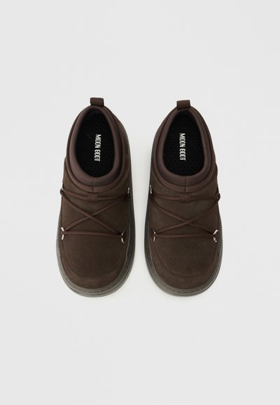 Zapatos marrones tipo mocasín con una textura similar al ante, con puntera redondeada, cordones elásticos y suelas de goma gris. El interior cuenta con un acolchado estampado.