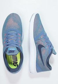 Modré a šedé sportovní boty s texturovaným síťovaným svrškem, růžovými akcenty a polstrovanou bílou podrážkou s černým logem Nike.