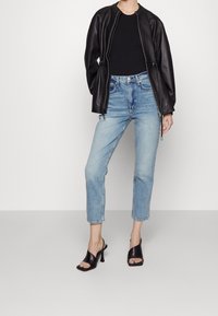 Chaqueta bomber de cuero negra, top negro, vaqueros de tiro alto en azul claro y sandalias negras de tacón alto con punta cuadrada.