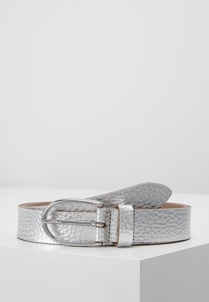 Ceinture en cuir texturé argenté avec une boucle métallique argentée arrondie reposant sur une surface blanche sur un fond clair uni.
