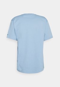 Light blue cotton t-shirt with a crew neckline and short sleeves. Features a subtle logo on the left sleeve. Smooth texture and relaxed fit.