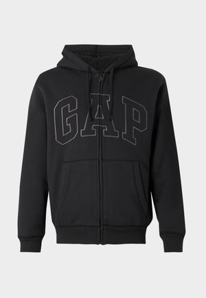 Black zip-up hoodie with front pockets, drawstring hood, and large stitched "GAP" logo across the chest, lined with soft fleece inside.
