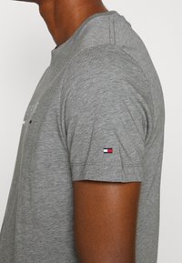 Närbild av en person som bär en grå kortärmad skjorta med en liten röd, vit och marinblå flagglogotyp på ärmen.