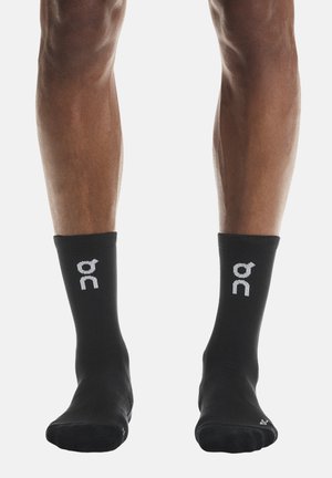 Șosete atletice negre cu textură striată, având un logo alb pe manșete, de lungime medie până la gambă, concepute pentru confort și susținere.