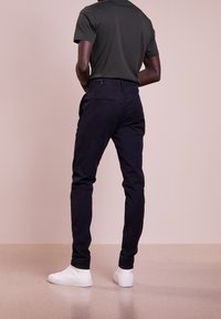 Pantaloni blu scuro in vestibilità slim, realizzati in tessuto morbido con tasche laterali. Abbinati a sneaker bianche, con una superficie liscia.