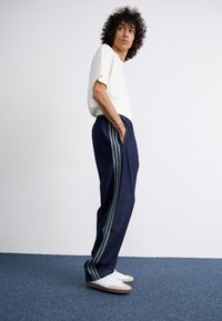 Navy blue pants with gray stripes along the sides, made from a smooth fabric. Paired with a light-colored, short-sleeve T-shirt and white sneakers.