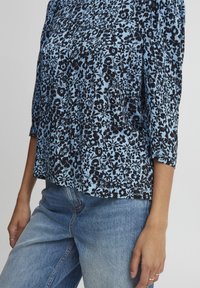 Camicia nera a fantasia floreale su sfondo azzurro, con maniche a tre quarti e vestibilità ampia, abbinata a jeans azzurri.