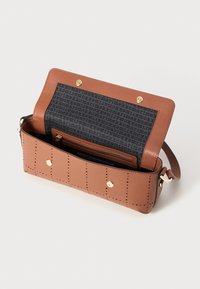 Väskan är en brun lädercrossbody med perforerat mönster, gold hardware, magnetisk snäpplåsning, och ett svart mönstrat foder med en dragkedjeficka.