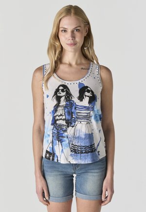 Mujer con camiseta sin mangas blanca con un boceto azul y negro de dos mujeres elegantes con gafas de sol, combinada con shorts de mezclilla enrollados.