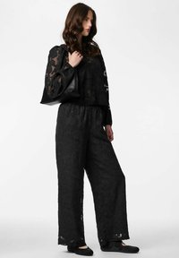 Mustast lillemustriga läbipaistev pluus, kombineeritud lahtiste mustade pükstega. Komplekti kuuluvad tekstuuriga kangas ja lihtne must käekott.