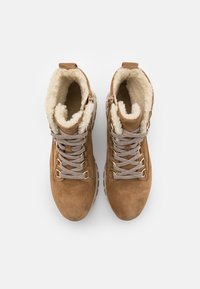 Kozaki zamszowe w kolorze tan z futerkiem, jasnoszare sznurówki i teksturowana podeszwa. Wysoka cholewka z bocznymi zamkami i miękkim wnętrzem.