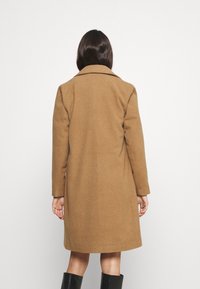 Abrigo de lana marrón con un cuello clásico, mangas largas y silueta estructurada, que llega hasta la mitad de la pantorrilla. Textura suave y detalles mínimos.