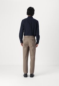 Námořnická košile na knoflíky s límečkem, spárovaná s béžovými kalhotami, obě z hladké tkaniny. Černé boty dokončují outfit.