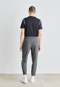 Sportstøj bestående af en sort t-shirt og grå tætsiddende bukser. Bukserne har en elastisk talje og ankelmanchetter. Hvide sneakers er synlige.
