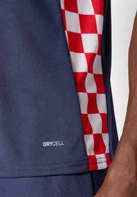 Marinblå sportskjorta med ett rödvitt rutmönster på sidan, tillverkad av fuktavledande DryCell-material.