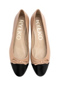 Ballerines en cuir beige avec un bout noir, dotées d'un petit nœud sur le devant. Texture lisse avec une forme arrondie.
