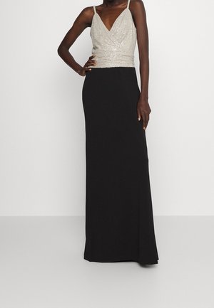 Ärmelloses Abendkleid mit einem funkelnden silbernen Wickel-Oberteil und einem langen, geraden schwarzen Rock, getragen von einer stehenden Person.