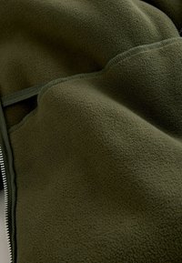 Olive green fleece fabric with a textured surface, featuring a zipper and lined edges. The fabric appears soft and insulated.