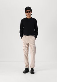 Sort ribbet langærmet sweater parret med lyse beige corduroy cargo bukser med to sidelommer, afsluttet med sorte snørebåndssko.