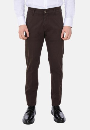Pantaloni in cotone marrone con vestibilità slim, dotati di chiusura frontale con bottone, tasche laterali e texture liscia. Indossati con scarpe nere lucide.