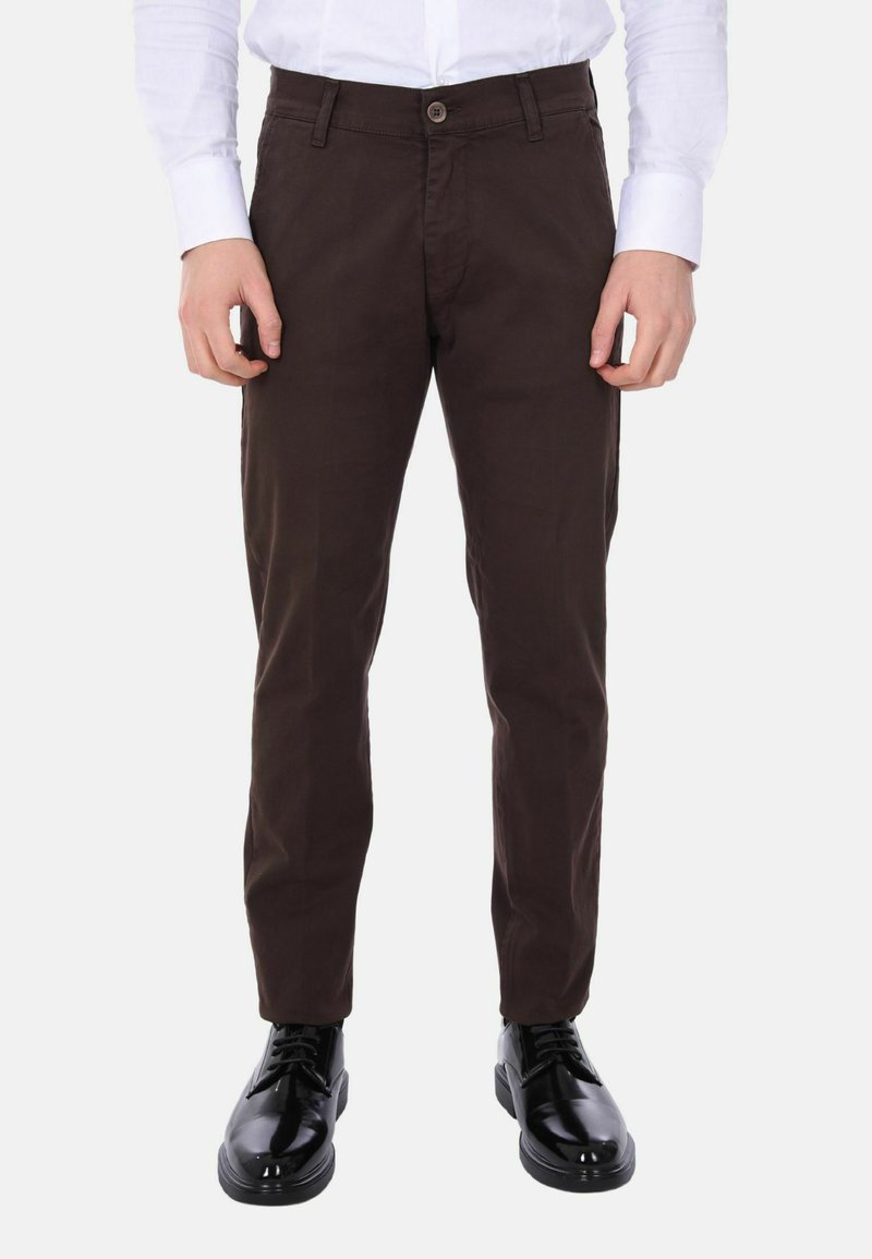 Pantaloni in cotone marrone con vestibilità slim, dotati di chiusura frontale con bottone, tasche laterali e texture liscia. Indossati con scarpe nere lucide.