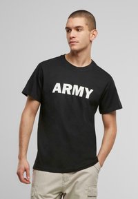 Juodas medvilninis marškinėliai su dideliu baltu „ARMY“ užrašu priekyje, trumpomis rankovėmis ir apvalia iškirpte. Kasdienis, laisvai krentantis dizainas.