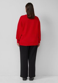 Rode geribbelde trui met een losse fit en lange mouwen, gecombineerd met zwarte wijde broek. De textuur is soepel en comfortabel.