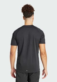 Camiseta negra de manga corta con escote redondo, que presenta mangas raglán y acentos blancos a lo largo de los hombros. Textura de tejido suave.