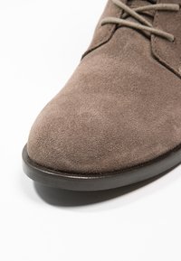 Braune Wildlederschuhe mit runder Zehenform und grauen Schnürsenkeln. Verfügt über eine schwarze Gummisohle und eine glatte Textur auf der Oberseite.