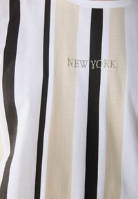 Striped T-shirt featuring alternating white, beige, and black vertical stripes. "NEW YORK" is embroidered in gold thread on the front.