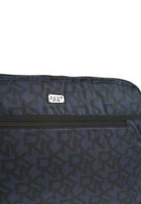 Bolsa de nylon negra con un patrón repetitivo de logotipos "DKNY" en gris oscuro, que cuenta con un cierre de cremallera y una etiqueta de logotipo plateada. Textura suave.