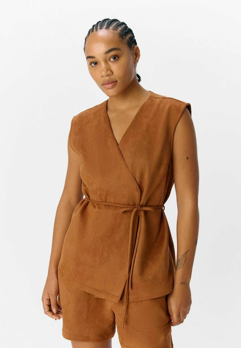 Haut enveloppant sans manches marron en tissu doux avec une ceinture à nouer à la taille, doté d'un décolleté en V et de bords arrondis.