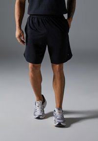 Svarte treningsshorts med elastisk midje og sidelommer, sammen med grå og svarte joggesko med lagdelte design.
