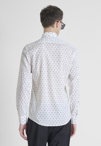 Camicia bianca a maniche lunghe con piccoli motivi geometrici neri, colletto alla coreana e orlo curvo. Tessuto in cotone morbido con una vestibilità su misura.