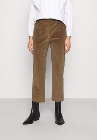 Bruine corduroy broek met een rechte pijp, voorzien van een middelhoge taille en twee zijzakken, gecombineerd met zwarte spitse enkellaarsjes.
