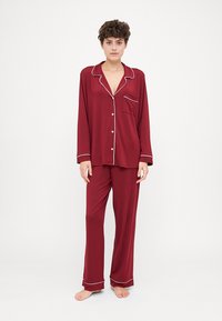 Burgundy pajama set featuring a button-up top with a pocket and contrast white piping, paired with loose-fitting, elastic waistband pants.