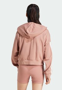 Roza skrajšana kapuca s kapuco, z ribanim robom in belimi stranskimi črtami. V kombinaciji s skrajšanimi roza hlačami, obema iz gladkega in raztegljivega materiala.