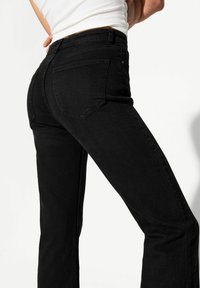 Schwarze Jeans aus Denim mit einer eng anliegenden Passform, geraden Beinen und zwei Gesäßtaschen. Der Stoff hat ein glattes, leicht strukturiertes Erscheinungsbild.
