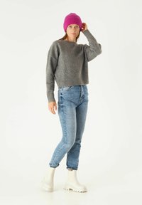 Grijze cropped trui, lichtblauwe jeans en witte enkelboots. Model draagt een felroze ribgebreide beanie. Casual, gelaagd outfit.