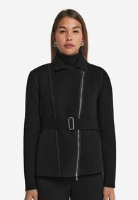 Svart ullblandad jacka med en strukturerad passform, som har en dragkedja framtill, hög krage och ett bälte i midjan. Accenterad med kontrasterande sömmar.