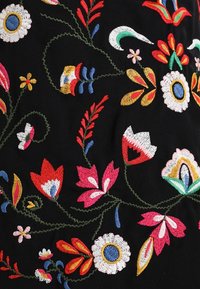 Tissu noir avec des fleurs et des feuilles brodées colorées en rouge, rose, blanc, jaune, bleu et vert, présentant des points détaillés et des tiges courbes.