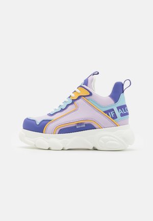Colorful sneaker featuring a mix of lavender, purple, yellow, and blue materials, chunky white sole, and textured accents.