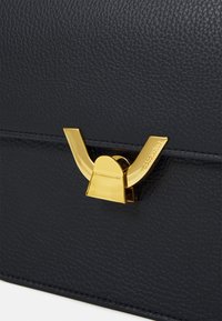 Schwarze Lederhandtasche mit strukturierter Oberfläche, goldener dekorativer Verschluss und präzisem Nähen entlang der Kanten.