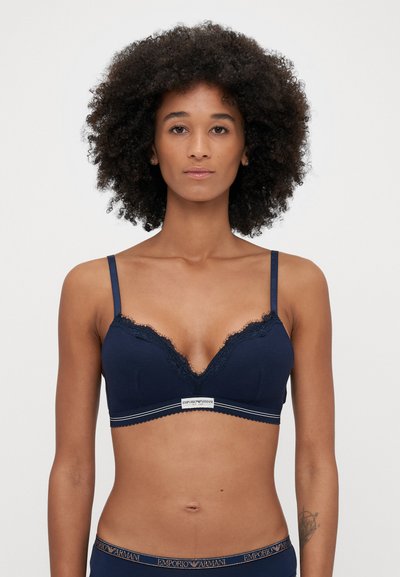 Marineblå bralette med blondedetaljer, justerbare stropper og elastisk bånd, med et logo i midten. Blød tekstur, trekantet form.