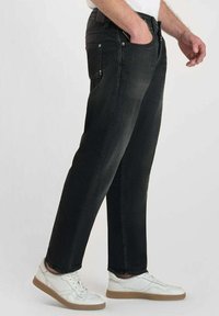 Jean en denim noir avec une coupe droite, cinq poches et un léger dégradé. Associés à des baskets blanches. Look minimaliste et décontracté.